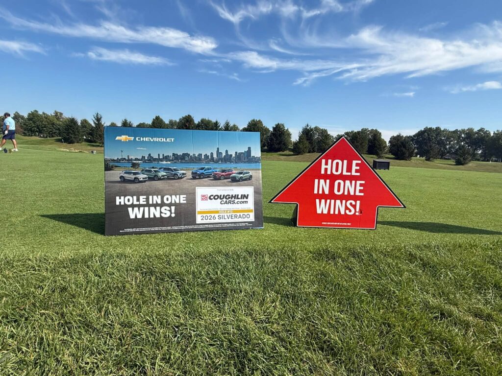 The Coughlin hole-in-one prize sign and 2026 Silverado board on the tee